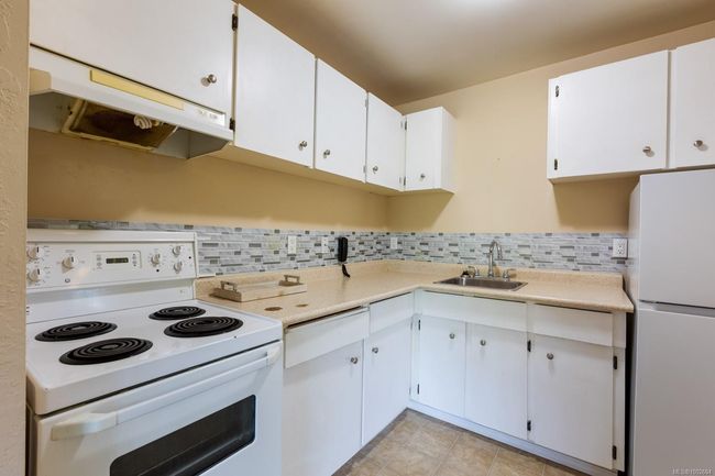Kitchen featuring white appliances, a sink, under cabinet range hood, light countertops, and decorative backsplash | Image 23