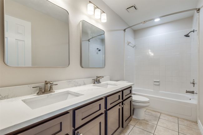 Bathroom with bathtub / shower combination, double vanity, tile patterned floors, and toilet | Image 18