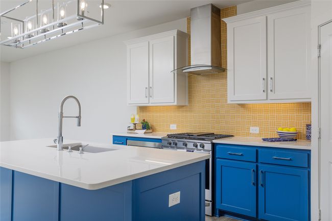 Kitchen with wall chimney range hood, stainless steel gas stove, blue cabinetry, decorative backsplash, and light countertops | Image 11