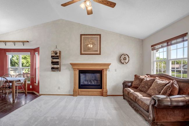 Carpeted living area featuring lofted ceiling, baseboards, a glass covered fireplace, ceiling fan, and wood finished floors | Image 5