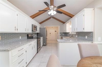 Kitchen with white cabinetry, kitchen peninsula, stainless steel appliances, vaulted ceiling with beams, and ceiling fan | Image 3