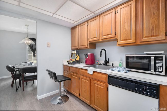 Kitchen with white dishwasher, light countertops, light wood finished floors, a paneled ceiling, and pendant lighting | Image 9