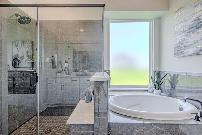 Enjoy spa-like luxury with a deep soaking tub and a sleek glass-enclosed shower wrapped in rich stone tile. | Image 26
