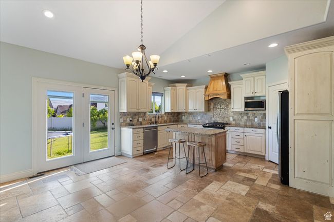 Kitchen featuring cream cabinetry, appliances with stainless steel finishes, custom range hood, a chandelier, and decorative backsplash | Image 4
