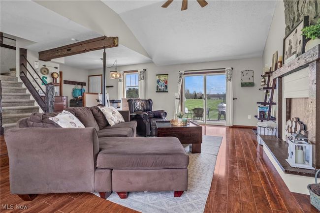 Living area featuring ceiling fan, dark wood-style flooring, a fireplace with raised hearth, stairway, and lofted ceiling | Image 12