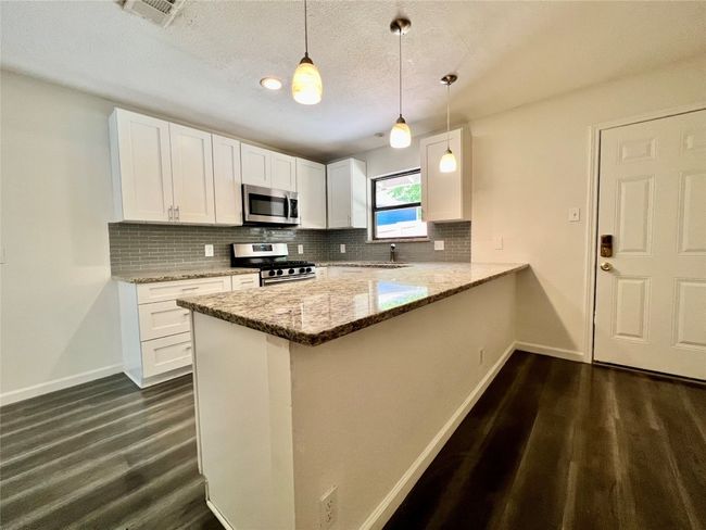 Kitchen featuring appliances with stainless steel finishes, baseboards, dark wood finished floors, backsplash, and light stone countertops | Image 8
