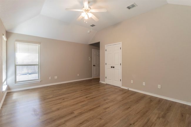 Empty room with lofted ceiling, wood finished floors, visible vents, baseboards, and ceiling fan | Image 22