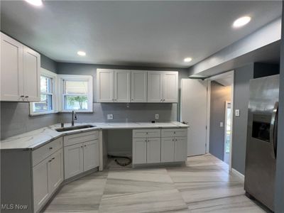 Kitchen featuring stainless steel fridge, decorative backsplash, white cabinetry, light stone counters, and sink | Image 2