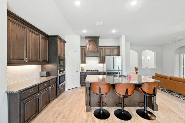 Kitchen featuring arched walkways, light wood-style floors, tasteful backsplash, a breakfast bar area, and light stone countertops | Image 13