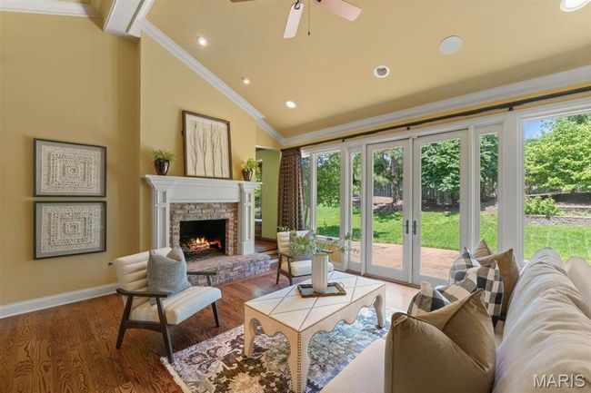 Living room with crown molding, lofted ceiling, a lit fireplace, ceiling fan, and wood finished floors | Image 5