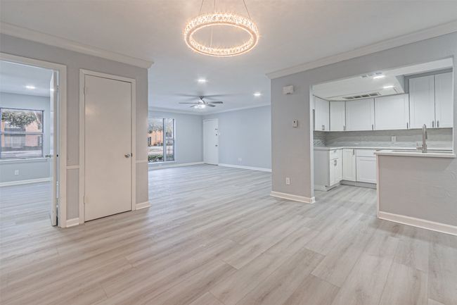 Unfurnished living room with ceiling fan with notable chandelier, plenty of natural light, ornamental molding, and light hardwood / wood-style floors | Image 18