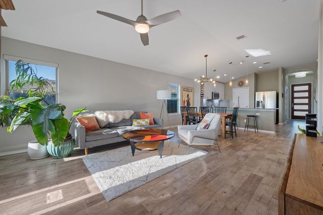 Living area with ceiling fan with notable chandelier, vaulted ceiling, visible vents, light wood finished floors, and baseboards | Image 8