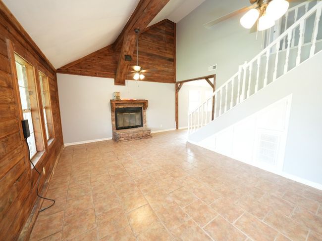 Unfurnished living room featuring ceiling fan, high vaulted ceiling, a fireplace, stairs, and beam ceiling | Image 10