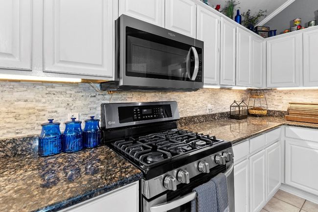 Kitchen with appliances with stainless steel finishes, white cabinetry, light tile patterned flooring, decorative backsplash, and dark stone counters | Image 16