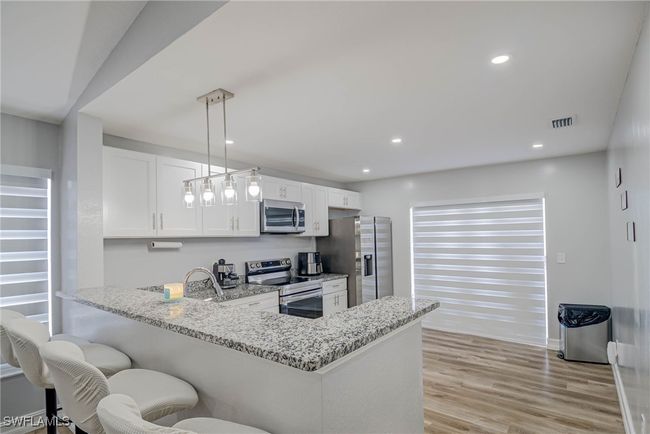 Kitchen featuring appliances with stainless steel finishes, a peninsula, white cabinetry, light stone counters, and recessed lighting | Image 7