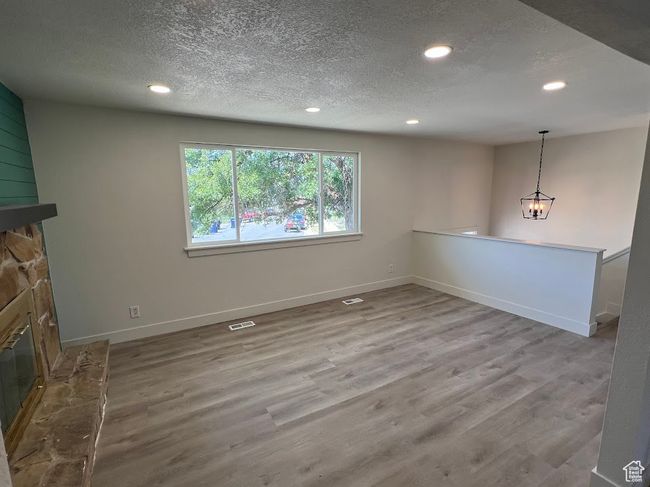 Unfurnished living room with a fireplace, recessed lighting, a textured ceiling, wood finished floors, and a chandelier | Image 6