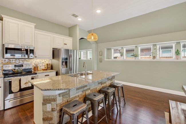 Kitchen featuring stainless steel appliances, light stone counters, decorative backsplash, a breakfast bar area, and white cabinetry | Image 14