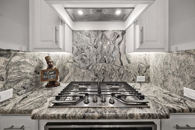 Kitchen with stainless steel gas cooktop, backsplash, white cabinetry, ventilation hood, and dark countertops | Image 9