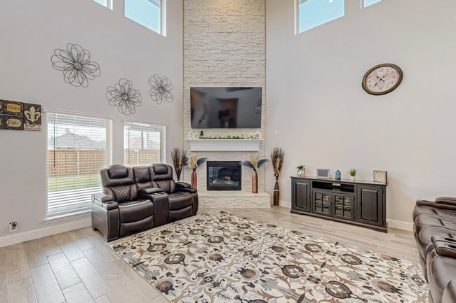 Living area featuring wood tiled floor, a fireplace, a towering ceiling, and baseboards | Image 4