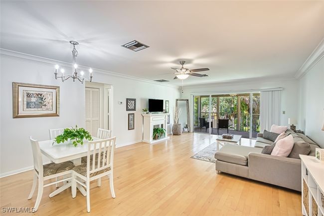 Living room with crown molding, light wood-style floors, a fireplace, ceiling fan, and a chandelier | Image 6