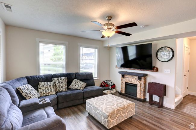 Living room with wood finished floors, a textured ceiling, visible vents, a ceiling fan, and a stone fireplace | Image 4