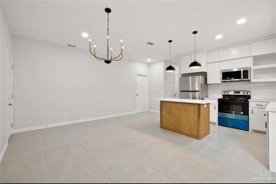 Kitchen featuring an inviting chandelier, white cabinetry, stainless steel appliances, decorative light fixtures, and a center island | Image 3