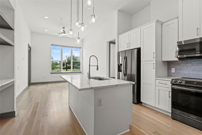 Kitchen featuring stainless steel appliances, a sink, backsplash, light stone counters, and an island with sink | Image 6