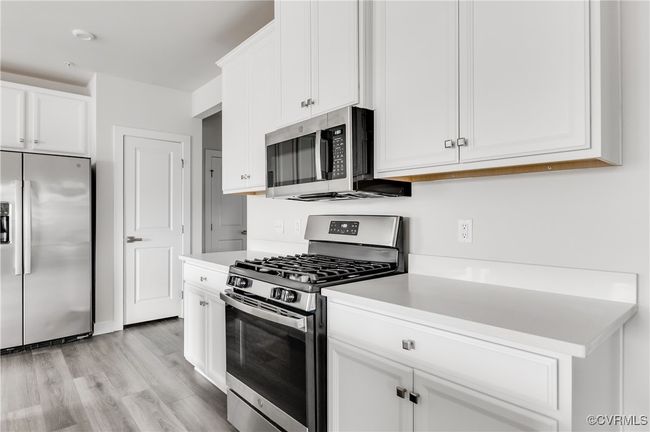 Kitchen with appliances with stainless steel finishes, white cabinetry, light countertops, and light wood-type flooring | Image 17