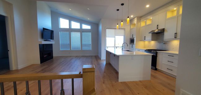 Kitchen with light wood-style floors, a kitchen island with sink, under cabinet range hood, and stainless steel appliances | Image 7