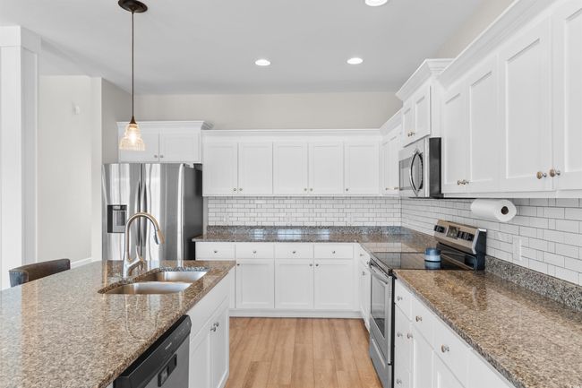 Kitchen featuring appliances with stainless steel finishes, white cabinets, hanging light fixtures, light wood-style flooring, and decorative backsplash | Image 10
