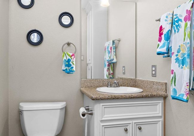 This is a compact bathroom featuring a single vanity with storage and a speckled countertop, a wall-mounted mirror, and a toilet. The space is accented with colorful towels and circular mirrors on the wall for a decorative touch. | Image 27