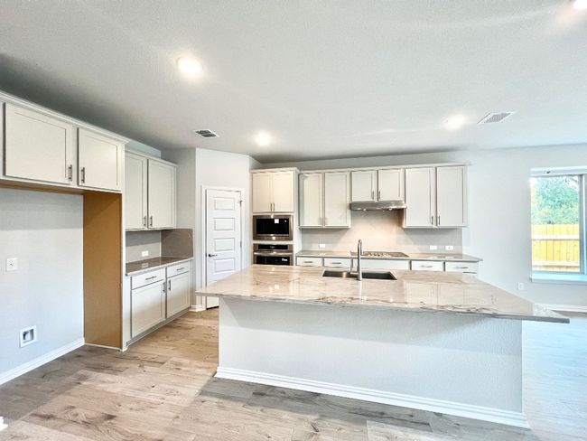 Kitchen featuring light stone counters, a center island with sink, light wood-type flooring, and tasteful backsplash | Image 10