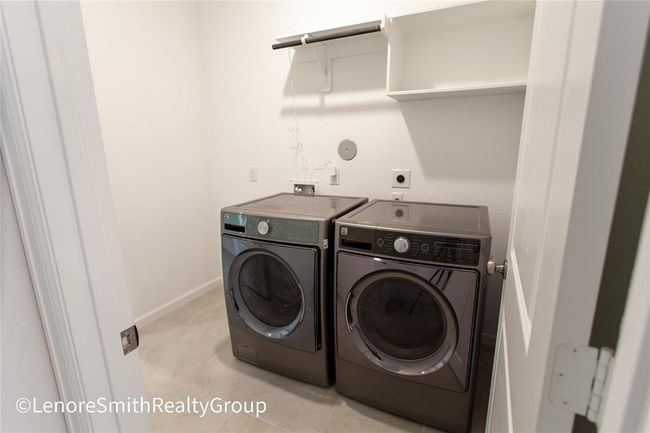 This modern laundry room is equipped with a sleek washer and dryer. The space features tiled flooring, and a shelf for storage. Appliances are negotiable | Image 12