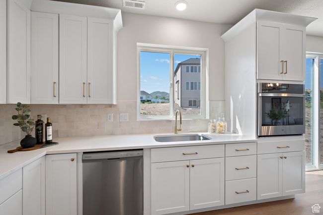 Kitchen with stainless steel appliances, white cabinetry, decorative backsplash, and light countertops | Image 12