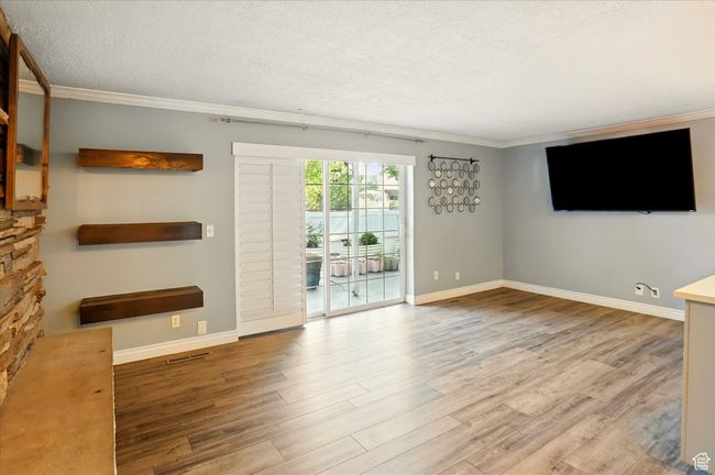 Unfurnished living room with crown molding, wood finished floors, baseboards, and a textured ceiling | Image 4