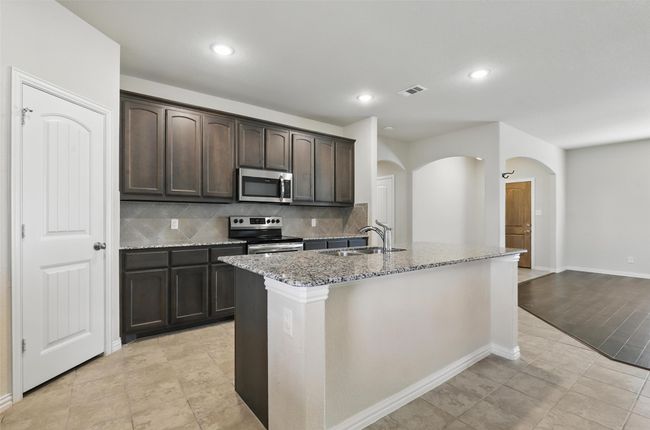 Kitchen featuring appliances with stainless steel finishes, a sink, arched walkways, light stone countertops, and tasteful backsplash | Image 9