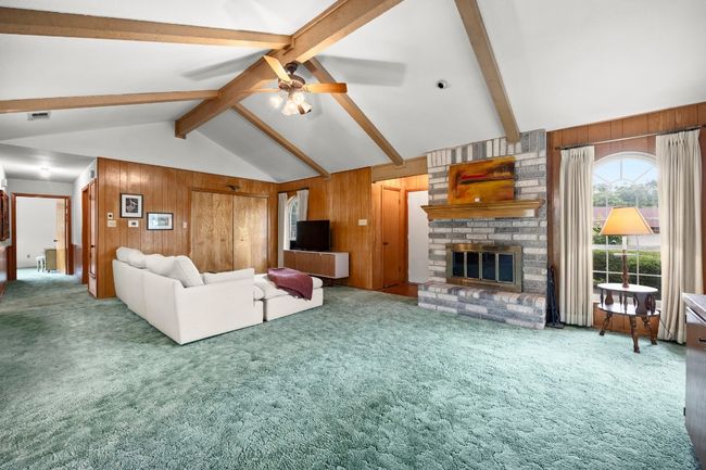 Carpeted living room featuring wood walls, a brick fireplace, and ceiling fan | Image 5