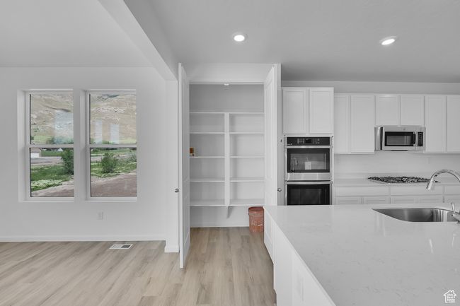 Kitchen featuring appliances with stainless steel finishes, light stone counters, white cabinets, light wood finished floors, and recessed lighting | Image 9