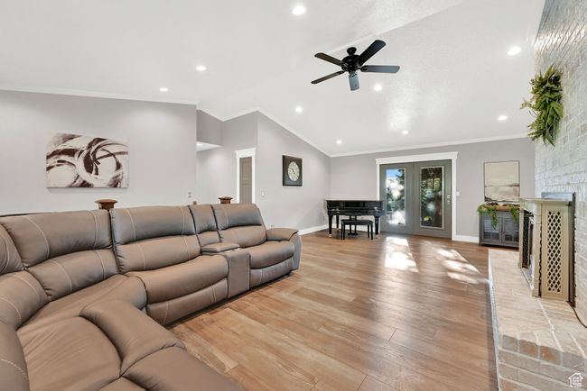 Living room with light hardwood / wood-style floors, a brick fireplace, crown molding, lofted ceiling, and ceiling fan | Image 8