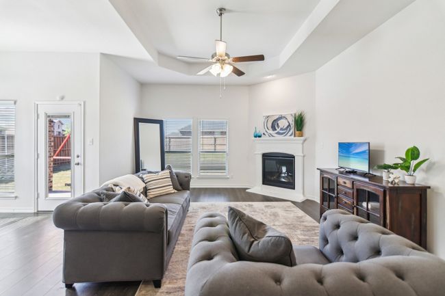 Living room with ceiling fan, a tray ceiling, a glass covered fireplace, wood finished floors, and baseboards | Image 4