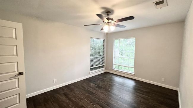 Spare room with ceiling fan, baseboards, dark wood-type flooring, and visible vents | Image 4