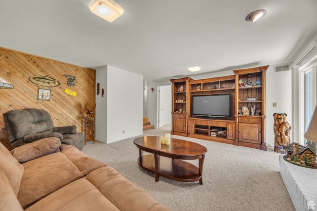 Living room with wooden walls, carpet, visible vents, and stairs | Image 21
