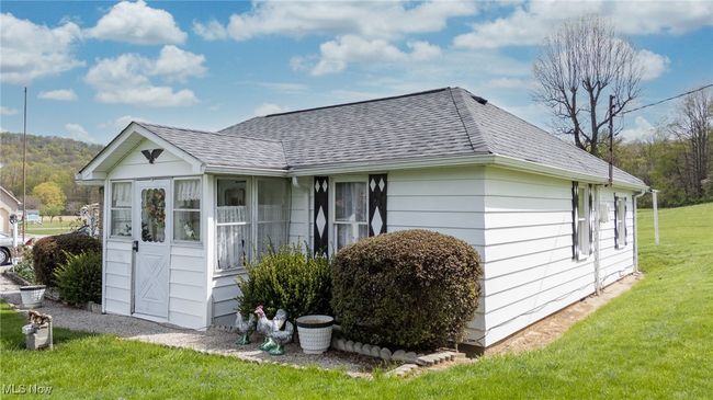 View of side of home featuring a shingled roof, a yard, and a sunroom | Image 39