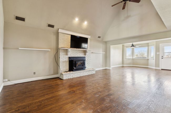 Unfurnished living room with ceiling fan, wood finished floors, visible vents, and high vaulted ceiling | Image 8