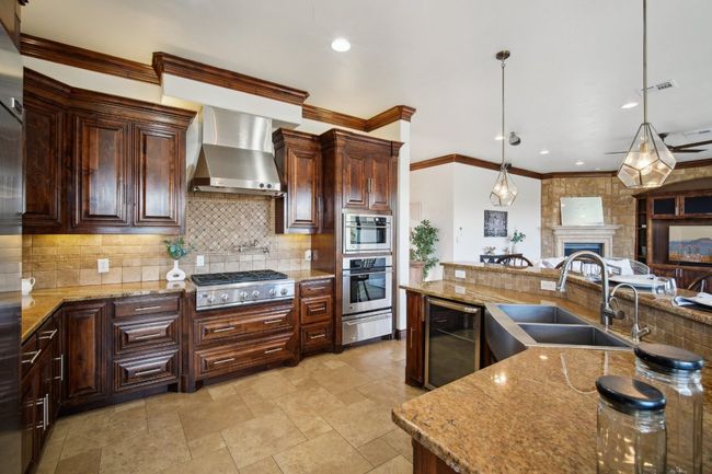 Kitchen featuring wall chimney range hood, stainless steel gas cooktop, beverage cooler, a warming drawer, and a sink | Image 16
