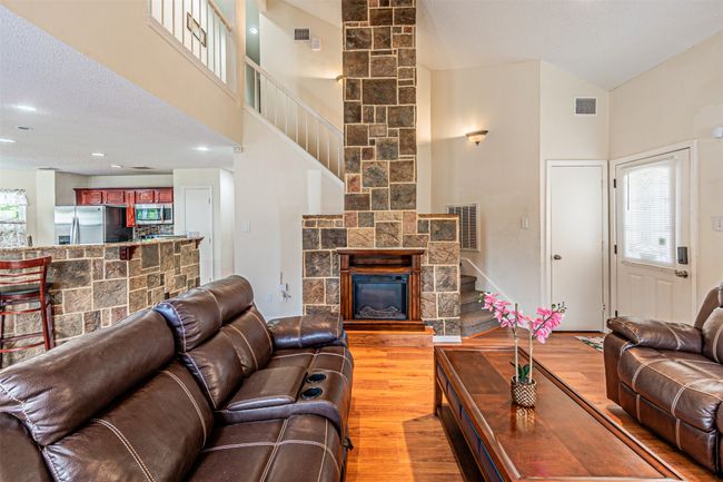 Living room with a high ceiling, light wood-style flooring, stairway, and a stone fireplace | Image 8