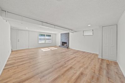 Basement featuring a textured ceiling, light hardwood / wood-style flooring, brick wall, and a brick fireplace | Image 3