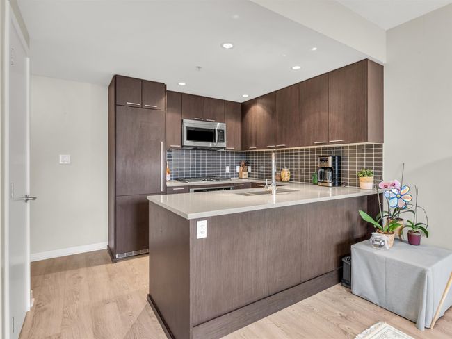 Kitchen with stainless steel appliances, light countertops, a sink, and light wood-style floors | Image 9