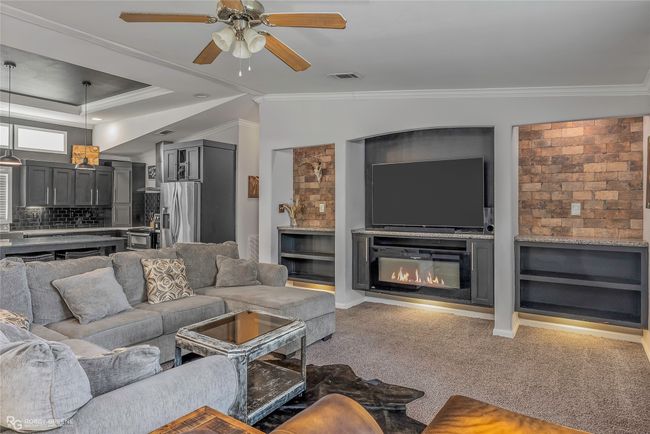 Carpeted living area featuring visible vents, ceiling fan, crown molding, and a glass covered fireplace | Image 10
