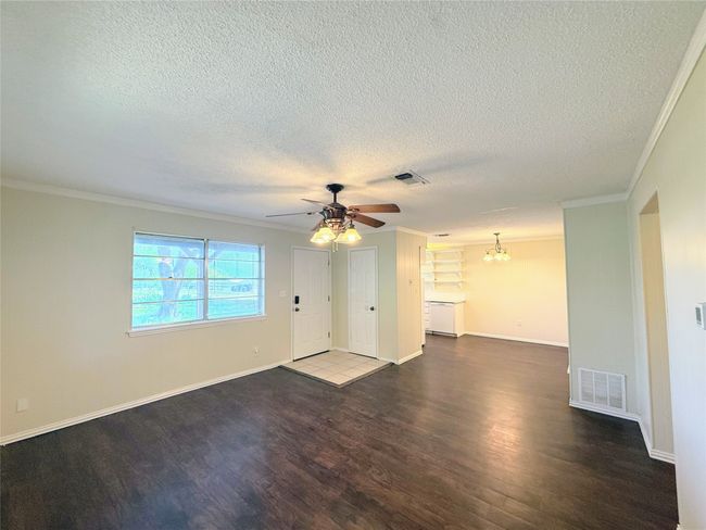 Unfurnished living room with ornamental molding, wood finished floors, a textured ceiling, ceiling fan, and a chandelier | Image 5
